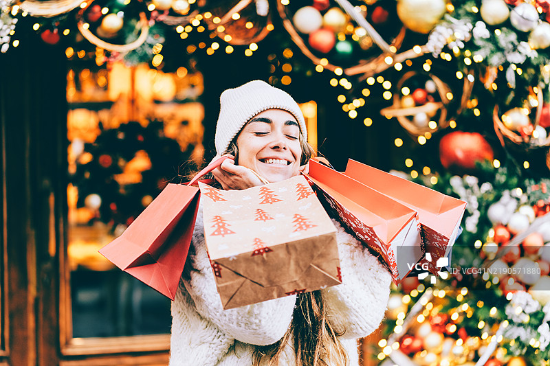 微笑的女性在圣诞季节户外购物，手里提着礼品袋图片素材