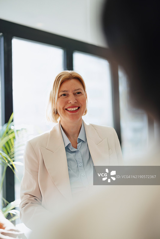 在明亮自然光下，微笑的职业女性在办公室会议中。图片素材