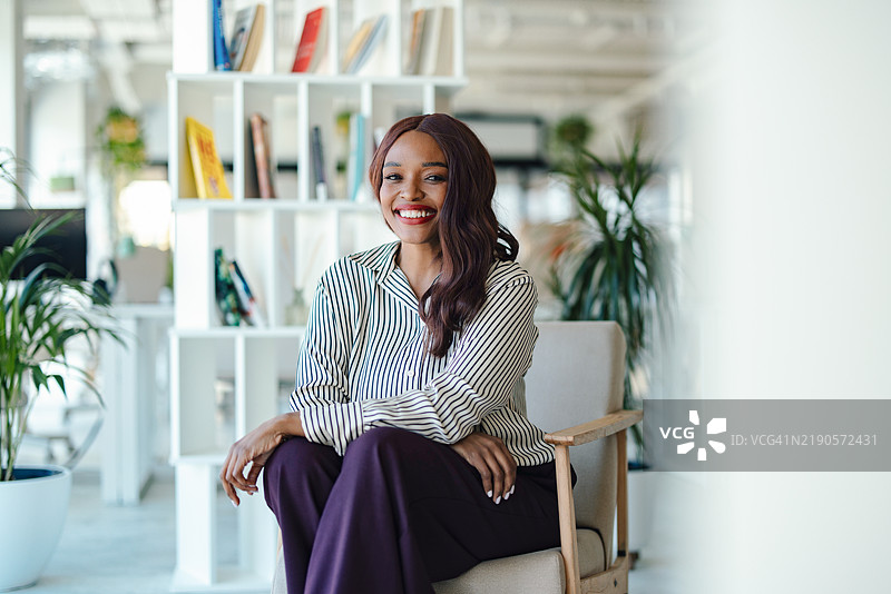 现代办公室环境中微笑的职业女性与绿色植物相伴图片素材