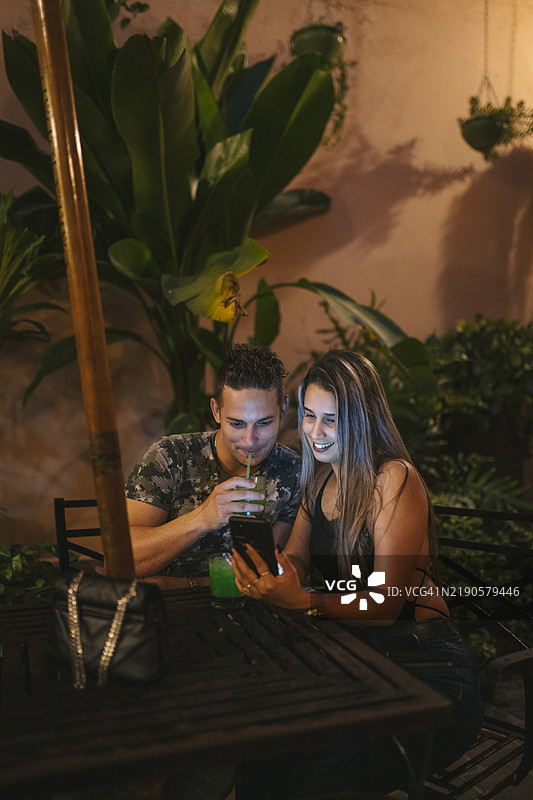 年轻情侣在古巴卡马圭看手机并喝鸡尾酒图片素材