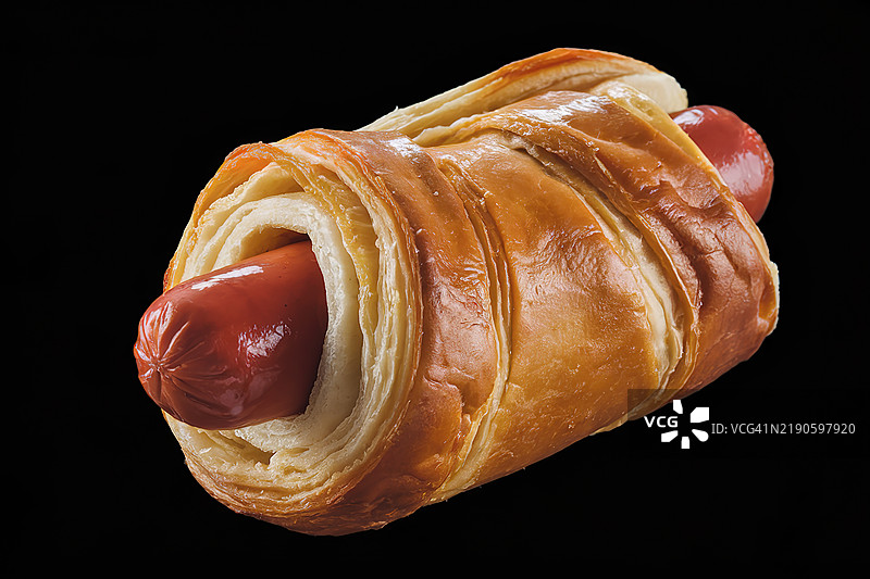 一张金棕色的糕点包裹着多汁的热狗的照片图片素材