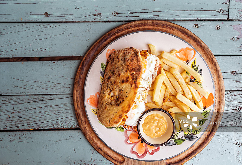 包含煎蛋、培根、猪肉香肠、融化的奶酪、牛肉饼、炸洋葱圈、西红柿和生菜的三明治，配有炸土豆，摆放在木桌上，哥伦比亚图片素材