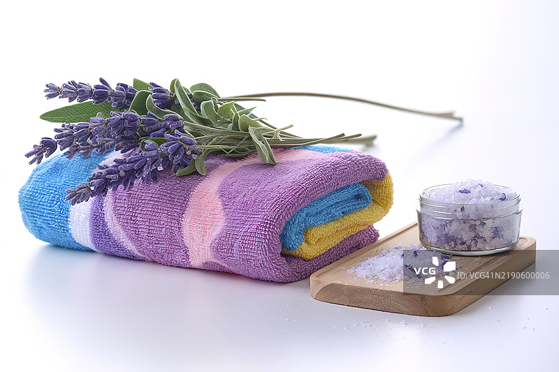 色彩斑斓的毛巾，上面有薰衣草花和芳香浴盐，背景为白色。图片素材