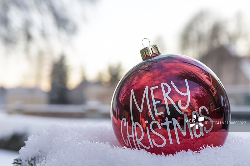 特写红色彩球，上面写着“圣诞快乐”，置于雪地上图片素材
