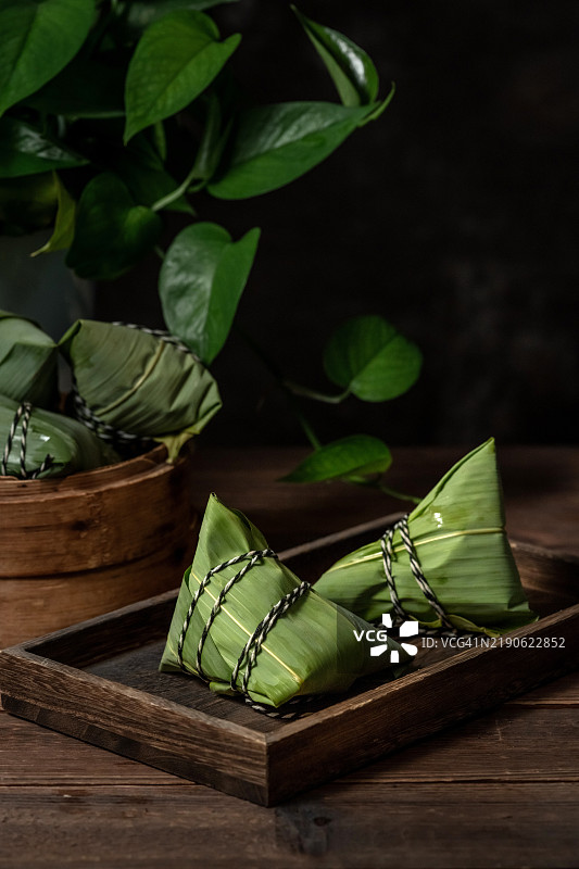 在昏暗的光线环境中，桌子上有绿色植物和一个小蒸锅里的粽子。图片素材