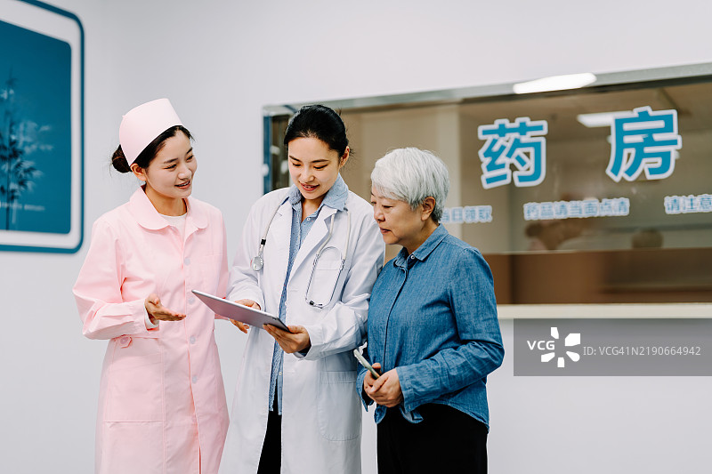美丽的女医生和护士在医院里与老年患者交谈，同时用数字平板解释医疗治疗。图片素材