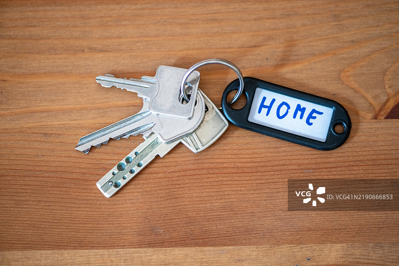 房屋钥匙放在木桌上，旁边有一个“家”的标签图片素材