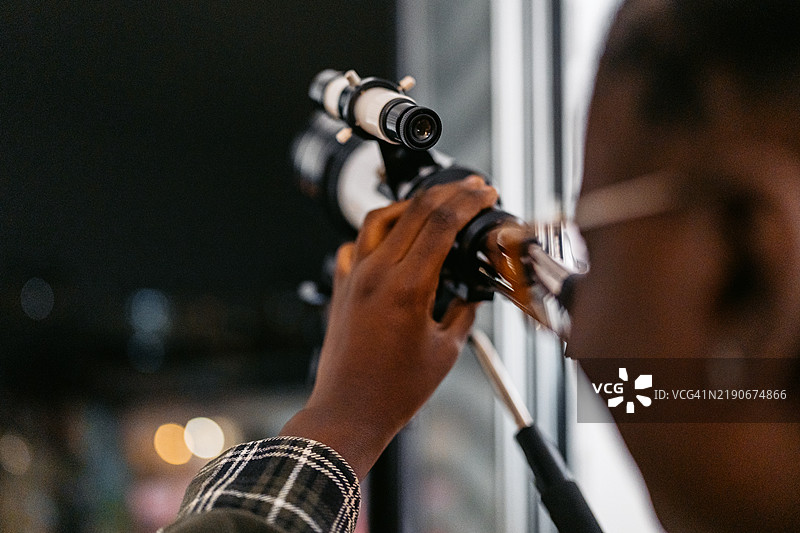 年轻的黑人女性在公寓里通过望远镜观察图片素材