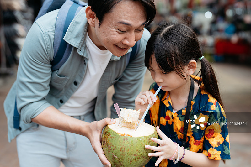父亲和女儿在马来西亚的亚洲街市上喝椰子水图片素材