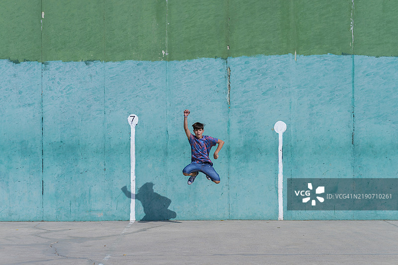 一个快乐的男孩在绿色墙壁前跳跃的正面视图图片素材