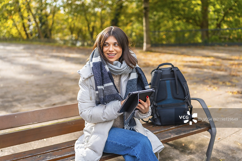 秋天阳光明媚的日子里，女人坐在公园长椅上使用平板电脑图片素材