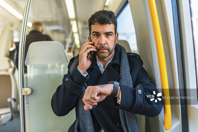 严肃的白人成年男性商务人士在地铁上使用智能手表并打电话的正面肖像图片素材