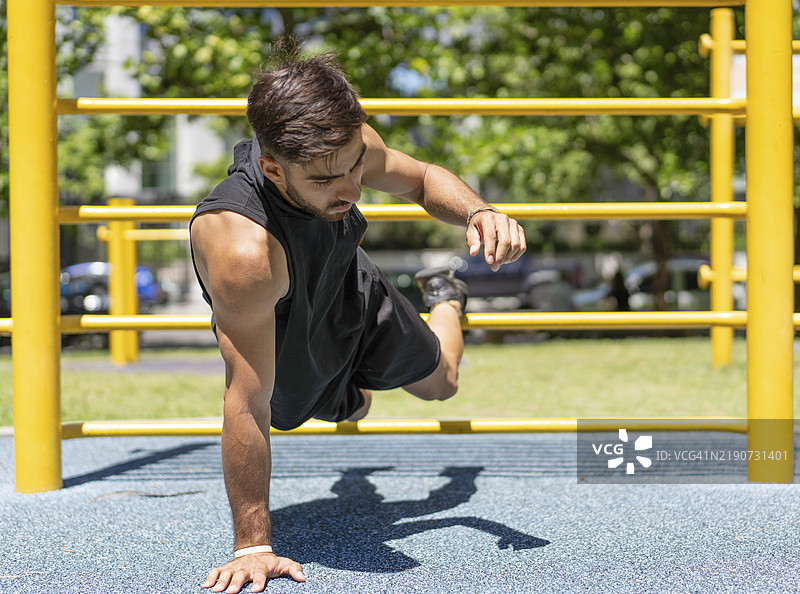 年轻男子在户外健身器材上做单手俯卧撑图片素材