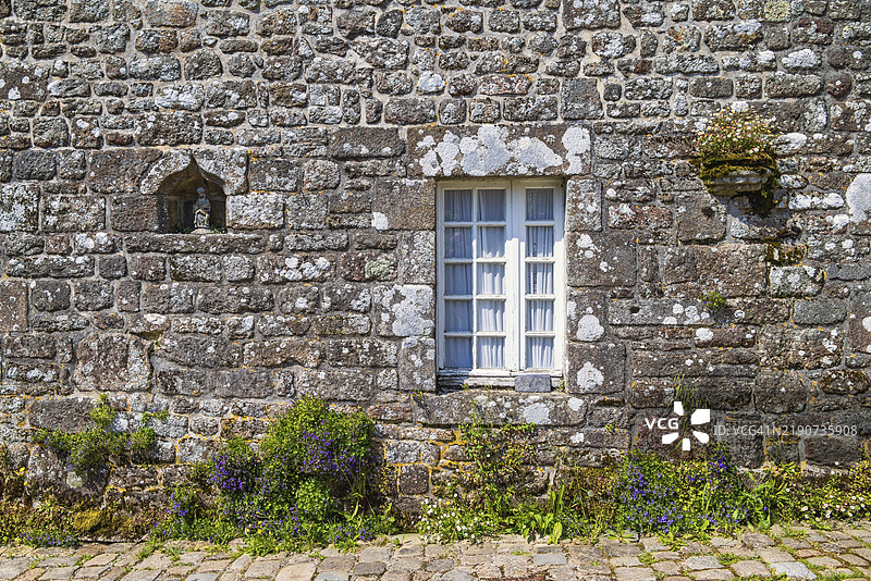 古老石屋的窗户，墙边开满鲜花，鹅卵石小路在阳光明媚的夏日里，位于法国布列塔尼的洛克罗南。图片素材