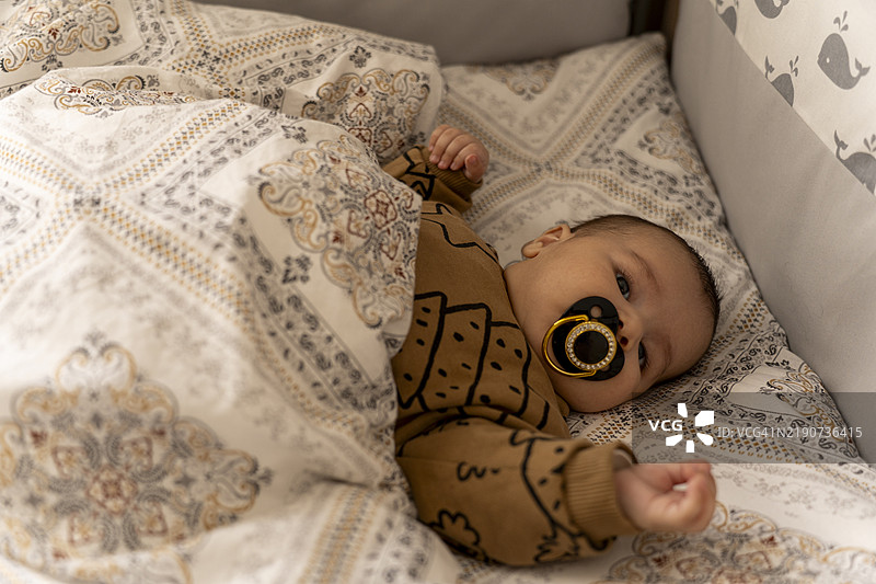 一个婴儿男孩躺在床上吮吸安抚奶嘴。图片素材