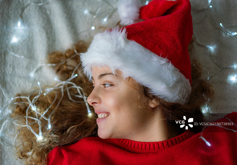 新年肖像：一位美丽的少女戴着新年帽，周围环绕着圣诞灯饰图片素材