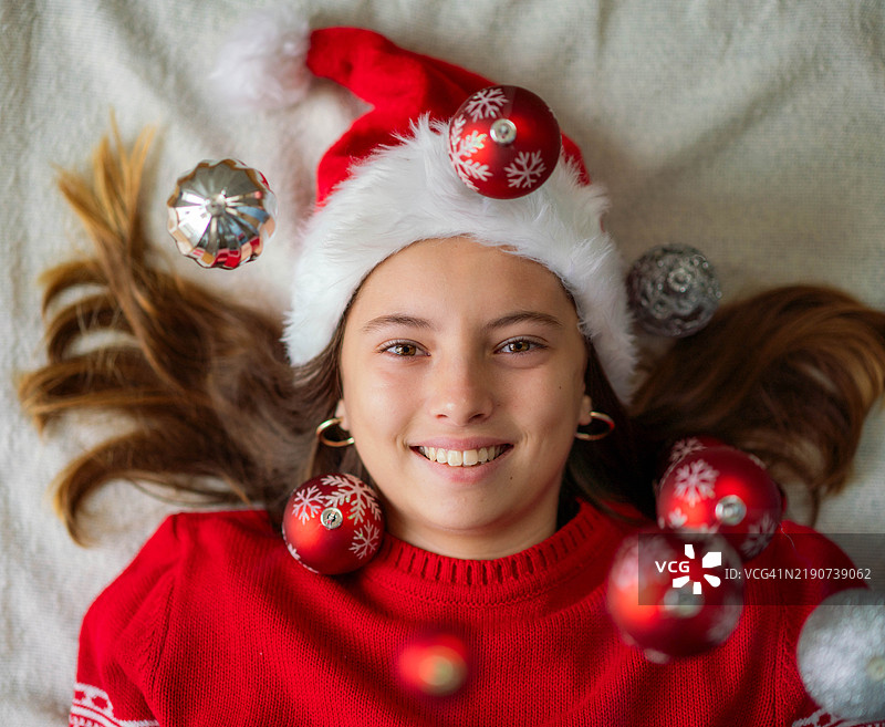 可爱的女孩穿着新年毛衣，玩弄新年装饰并做鬼脸。图片素材