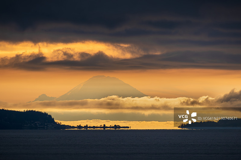 日出时分，雷尼尔山的壮观景色，乌云密布，前景是一片黑暗的海洋。图片素材