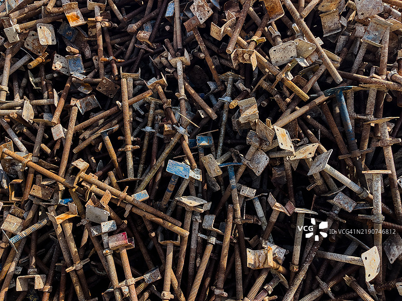 一大堆使用过的脚手架螺丝和底板，展示了生锈和风化表面的磨损建筑材料。图片素材