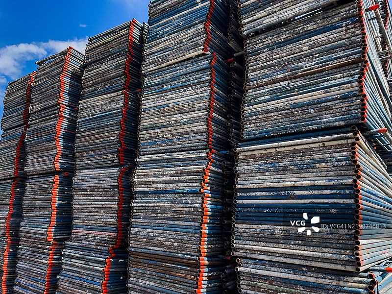 整齐排列在建筑工地上的高大金属脚手架管道，展示了在阳光明媚的天空下的工业材料。图片素材