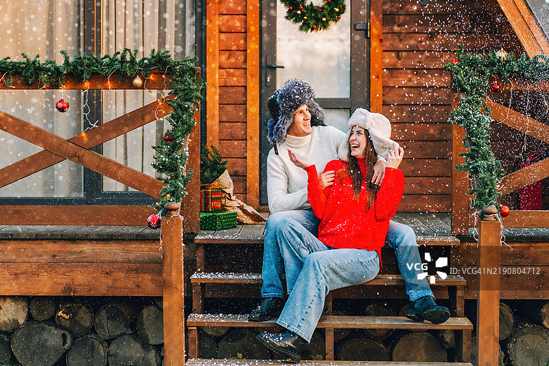 快乐的情侣戴着冬季帽子，在木质门廊上享受圣诞时光图片素材