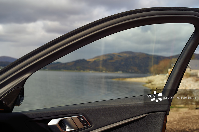 汽车车门打开，背景是宁静的湖泊和山脉，天空多云，苏格兰高地。图片素材