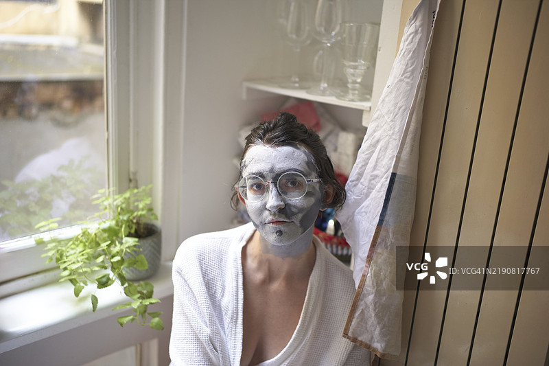 年轻女性在窗边带着面膜，面带宁静的表情图片素材