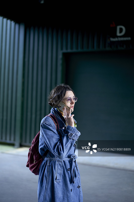 一位穿着牛仔外套的女性在绿色金属背景前打电话。图片素材