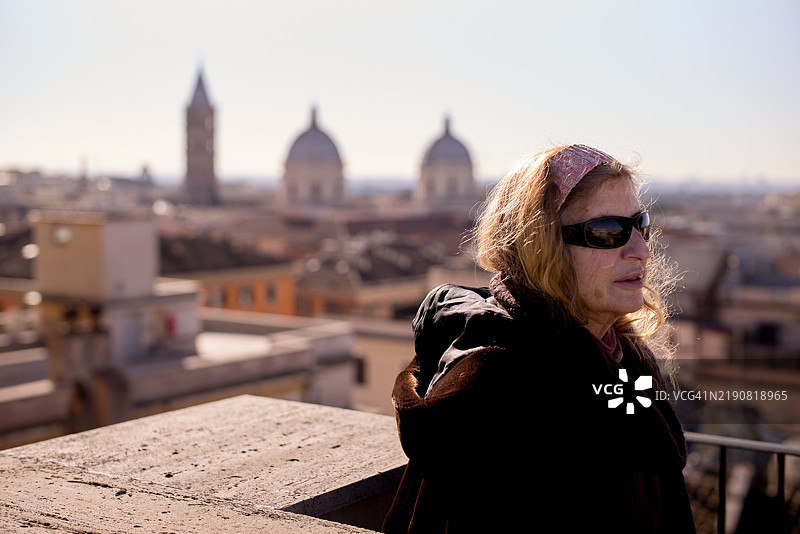 戴着太阳镜的女性俯瞰着历史建筑的城市风景，蓝天清澈，意大利罗马。图片素材