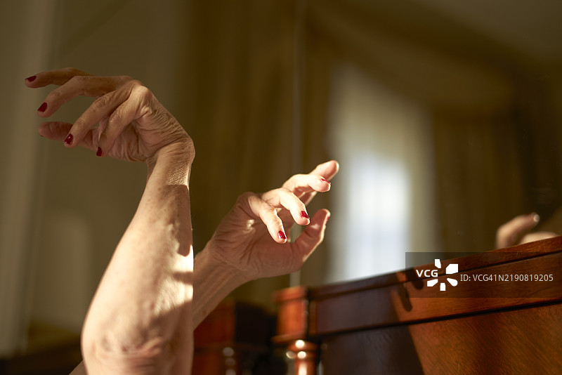 优雅的女性手指涂着红色指甲油，悬停在阳光明媚的房间内的木床框上，意大利罗马图片素材