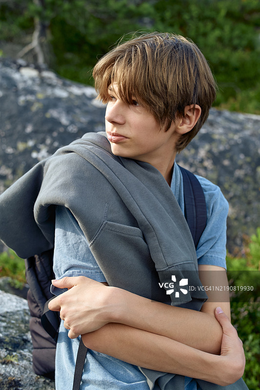 年轻的青少年在挪威罗姆斯达尔峡湾的徒步旅行中，肩上搭着一件夹克，背景是岩石。图片素材