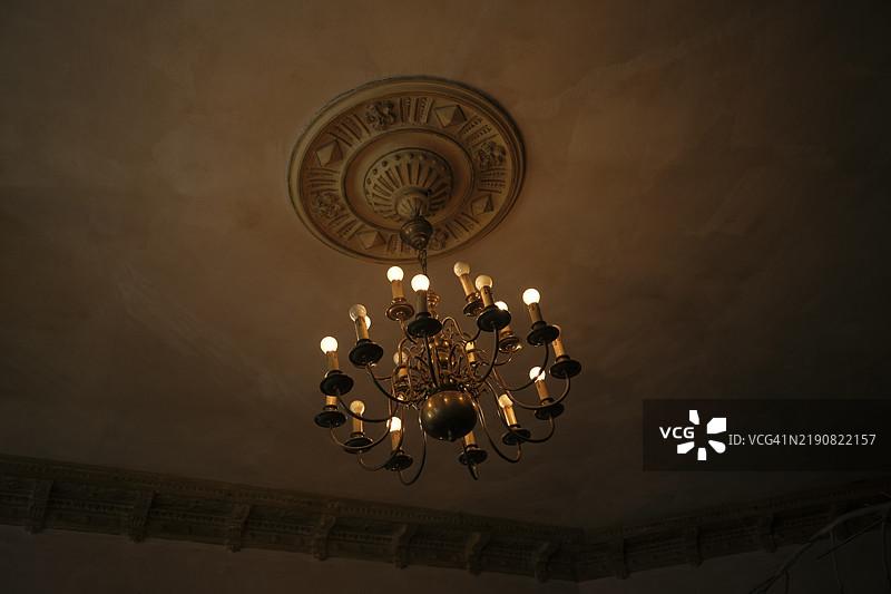 波兹南，波兰，昏暗房间内，点燃蜡烛的古董吊灯映衬着复杂的天花板装饰。图片素材