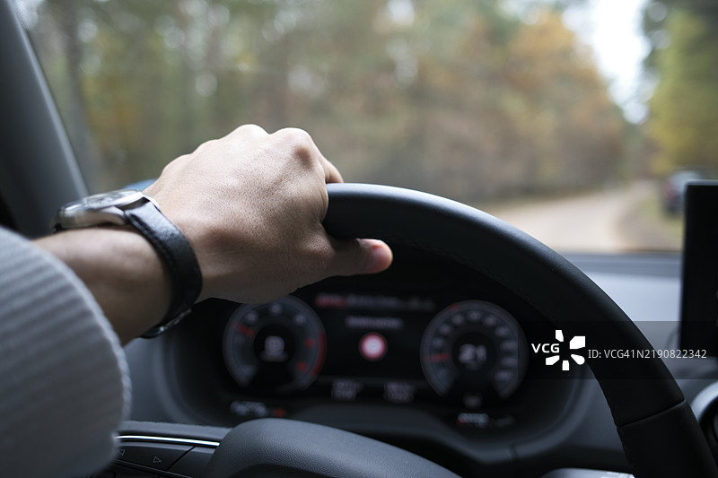 一个人手握方向盘的特写，汽车在林区行驶。图片素材