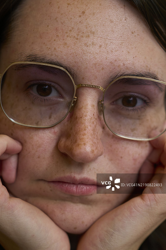 一位有雀斑的女性特写肖像，戴着圆形眼镜，轻柔地用双手托着脸庞，德国德累斯顿图片素材