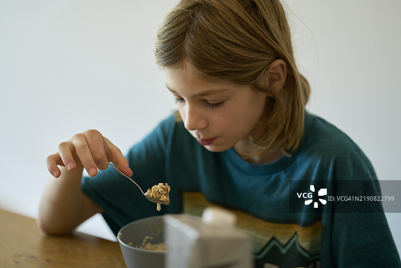 孩子在桌子上吃早餐麦片，手和勺子是焦点，德国图片素材
