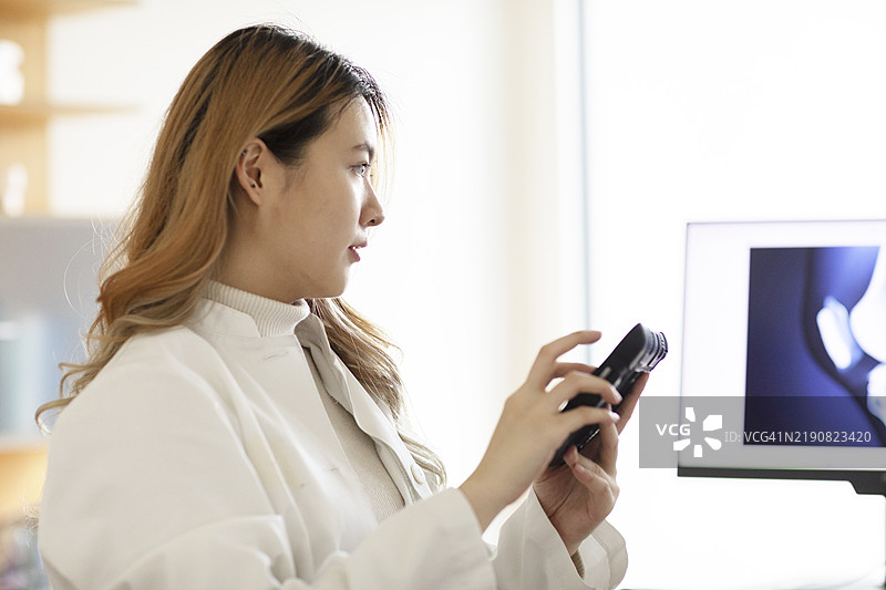 职业女性在明亮的办公室中检查相机，背景有一台电脑屏幕。图片素材