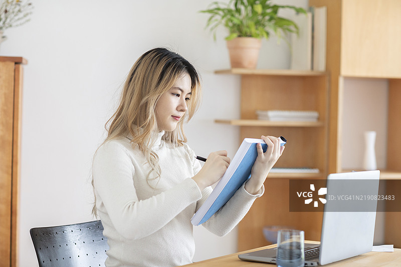 年轻女性在现代工作空间中从笔记本电脑上做笔记图片素材