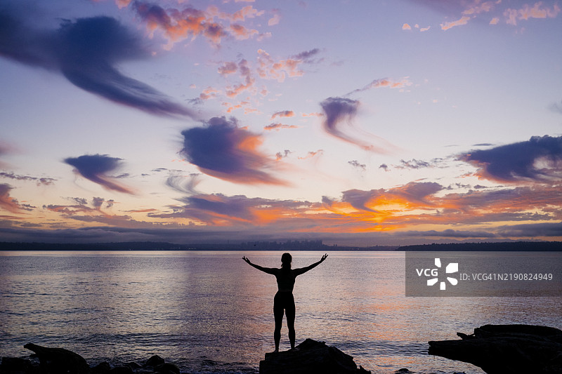 剪影中的女人双臂高举，背景是海洋上绚丽的日出图片素材