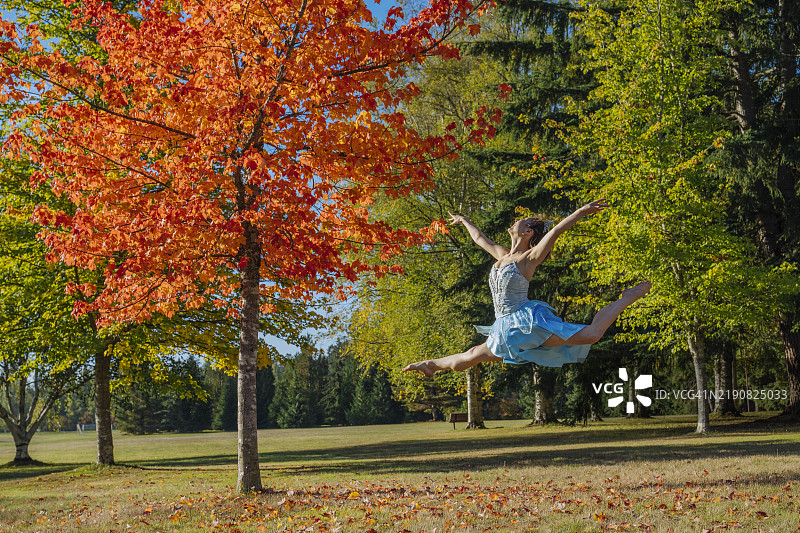 一位舞者在公园中优雅地跃起，背景是五彩斑斓的秋叶。图片素材