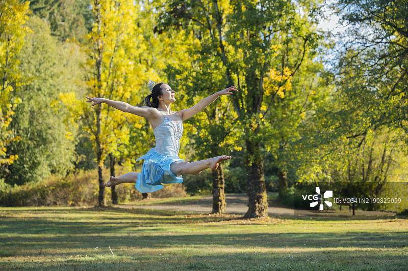 快乐的女人在阳光明媚的公园里跳舞，背景是秋天的树木图片素材