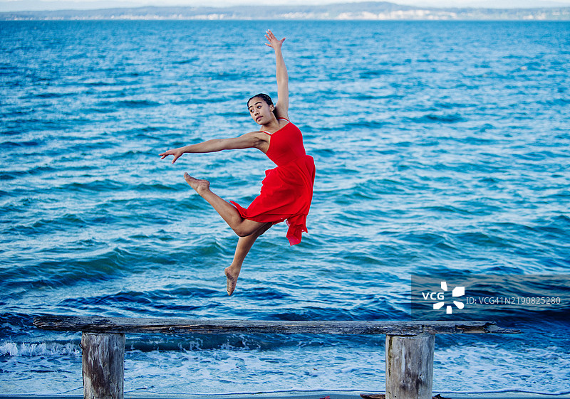 优雅的芭蕾舞者在海边的木栈道上跳舞，穿着鲜艳的红色裙子，美国图片素材