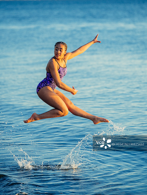 年轻女孩在日落时分的海滩上跳跃，双臂伸展，姿势顽皮，来自美国图片素材