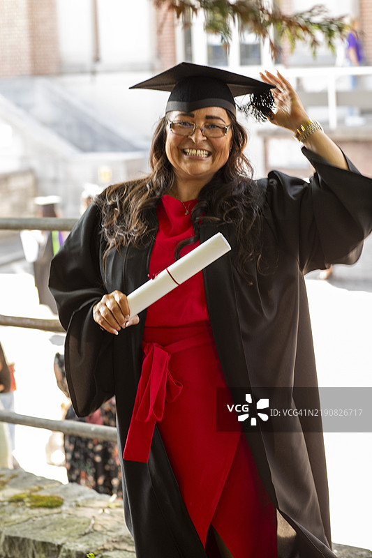 微笑的毕业生穿着学位服，手持文凭，在白天的户外，地点：英国多塞特郡博恩茅斯图片素材