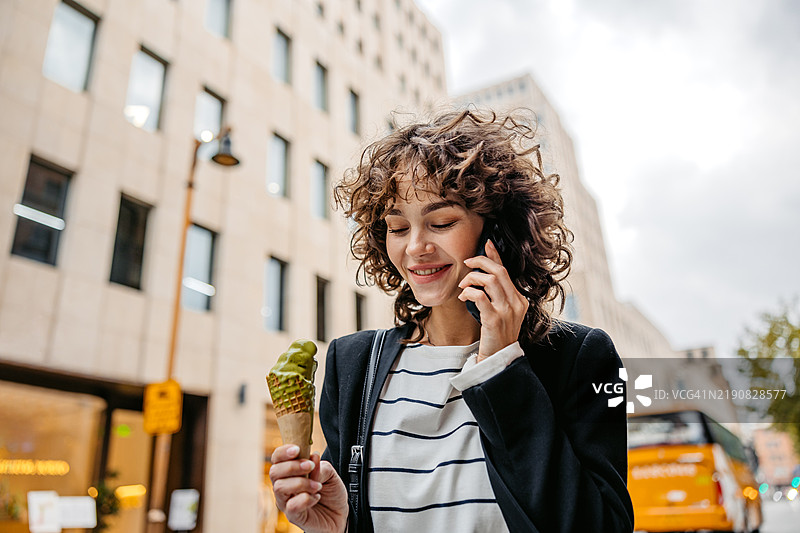 年轻女性在中国上海的街头一边吃开心果冰淇淋一边打电话图片素材
