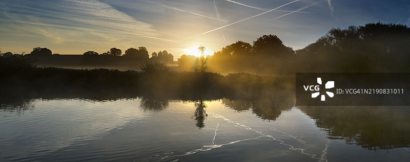 秋天黎明时分，拉德利船屋旁孤独的树木与泰晤士河的倒影图片素材