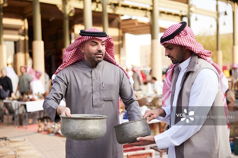 在跳蚤市场的摊位上，一对年轻情侣小心翼翼地挑选古董罐子，以丰富他们的收藏。图片素材