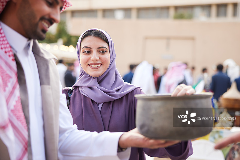 在跳蚤市场，夫妻俩仔细检查一个古董罐，欣赏其细节。图片素材
