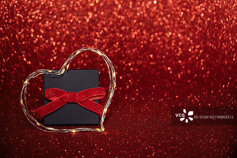 一个包裹着红色蝴蝶结的礼物盒被温暖的心形仙女灯环绕。图片素材