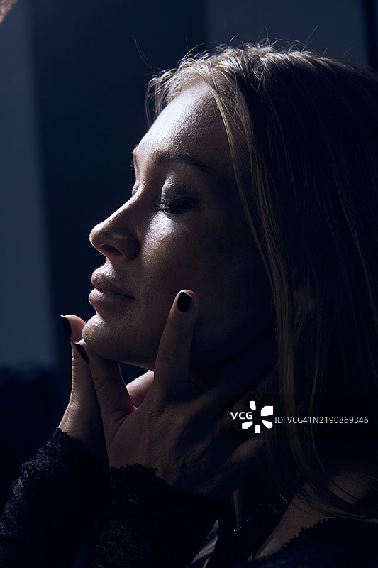 侧面肖像的女性。性感的女性在夜晚轻触她的脸庞。图片素材