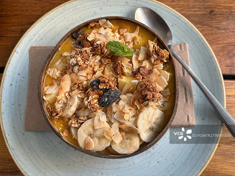 热带冰沙碗，配有菠萝、芒果、香蕉、百香果、烤椰子和格兰诺拉麦片，盛放在椰子壳碗中图片素材